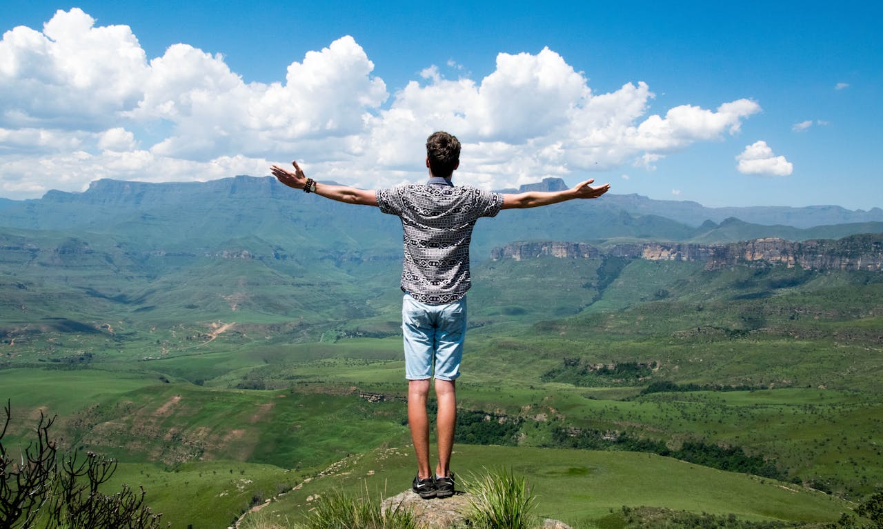 A man stands triumphantly with arms open, overlooking a scenic mountain range.