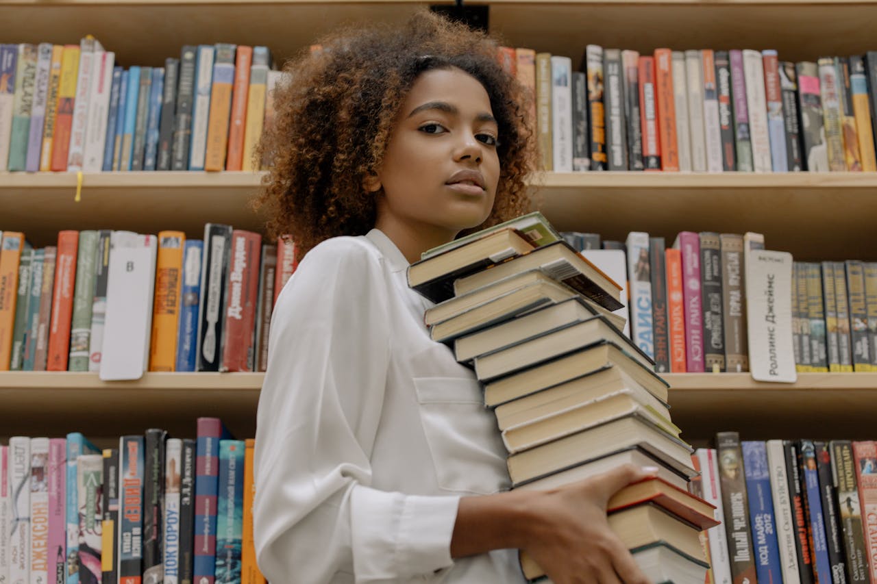 brand-02 Confident young woman holds stack of books in a library setting.